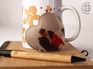 Herzförmige Acryl-Weihnachtskugel mit Foto – Größenvergleich neben weihnachtlicher Tasse und Kugelschreiber