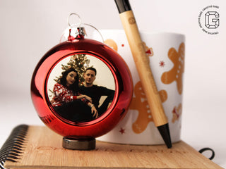 Personalisierte rote Christbaumkugel im Größenvergleich neben einer Tasse und einem Stift